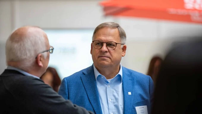 Ein Mann in blauem Sakko spricht mit einem anderen Teilnehmer bei einer Konferenz.