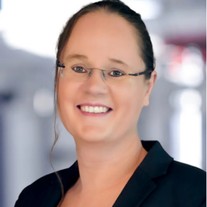 Porträt von Dr. Nadine Teusler, Netzwerkmanagerin, mit Brille und schwarzem Blazer, freundlich lächelnd vor verschwommenem Hintergrund.