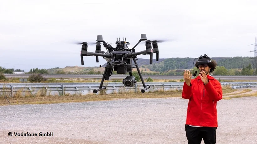 Mann mit AR-Brille in rotem Shirt steuert große Drohne auf Testgelände mit seinen Händen.