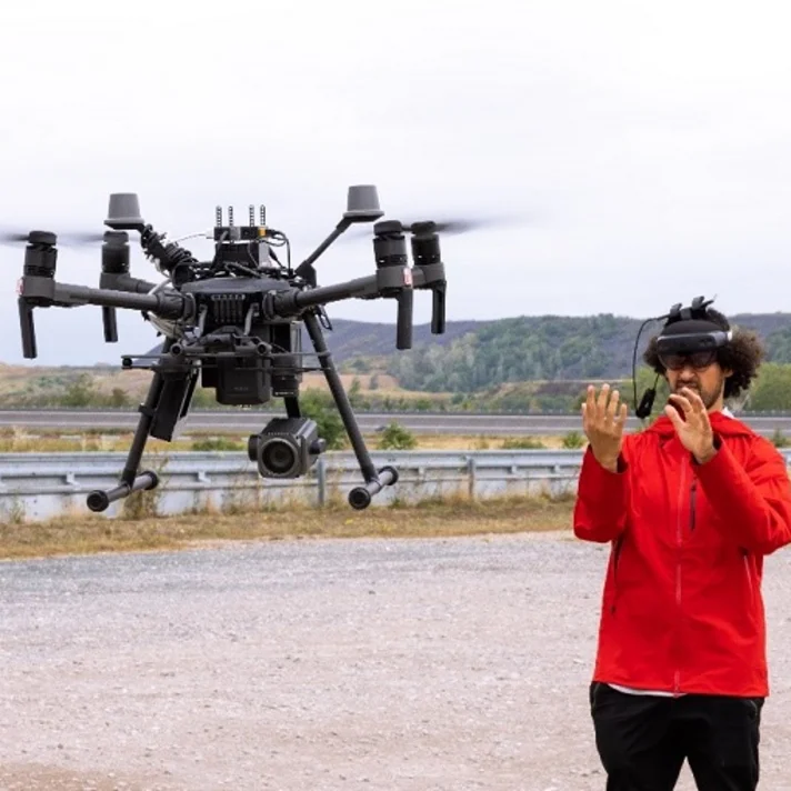 Mann mit AR-Brille in rotem Shirt steuert große Drohne auf Testgelände mit seinen Händen.