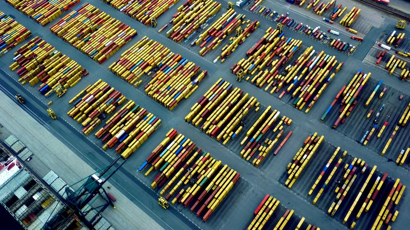 Luftaufnahme eines Hafens mit zahlreichen in Reihen angeordneten bunten Containern und Kränen