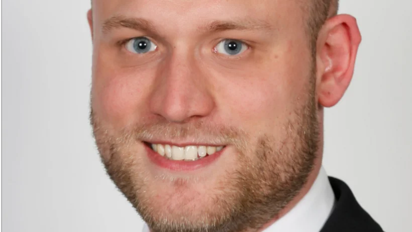 Portraitfoto von Malte Seifert, Director Metals & Autonomous Technologies XPONTENTIAL Europe, im Anzug mit Krawatte, der freundlich in die Kamera lächelt. Weißer Hintergrund mit abgerundeter schwarzer Rahmenkante.