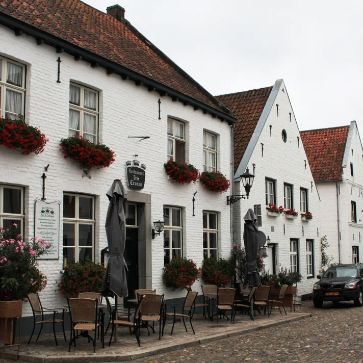 Straßenszene mit weiß verputzten Häusern, Blumenkästen an den Fenstern und Außengastronomie mit Tischen und Stühlen auf Kopfsteinpflaster