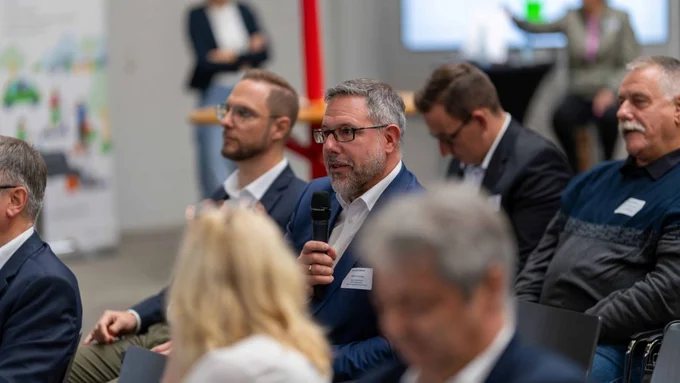 Mann im Anzug stellt mit Mikrofon eine Frage während einer Veranstaltung.