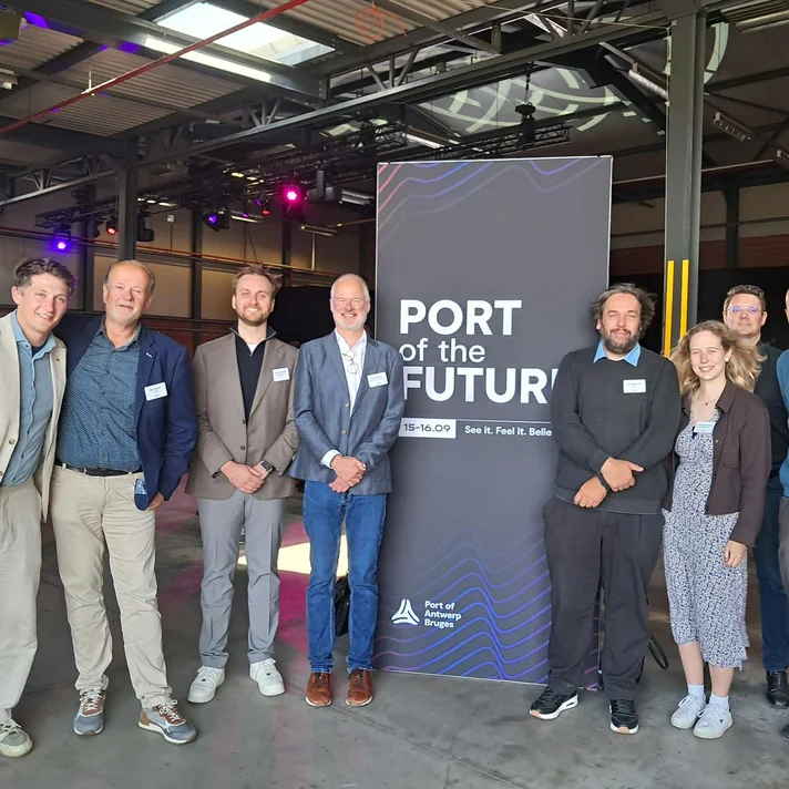 Sieben Personen stehen in einer Halle vor einem Banner mit der Aufschrift 'PORT of the FUTURE'