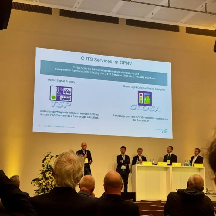 Podiumsdiskussion mit fünf Personen auf einer Bühne vor einer Präsentationsfolie zum Thema C-ITS Services im öffentlichen Nahverkehr.