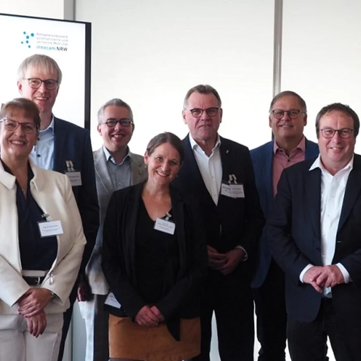 Gruppe von Personen bei einem offiziellen Termin vor einem Bildschirm mit dem innocam.NRW-Logo.