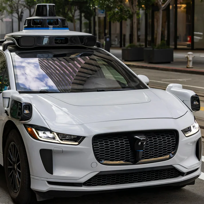 Weißes autonomes Auto mit Sensoren und Kameras auf dem Dach, steht auf einer Straße in der Stadt.