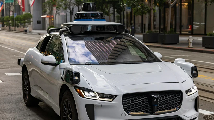 Weißes autonomes Auto mit Sensoren und Kameras auf dem Dach, steht auf einer Straße in der Stadt.
