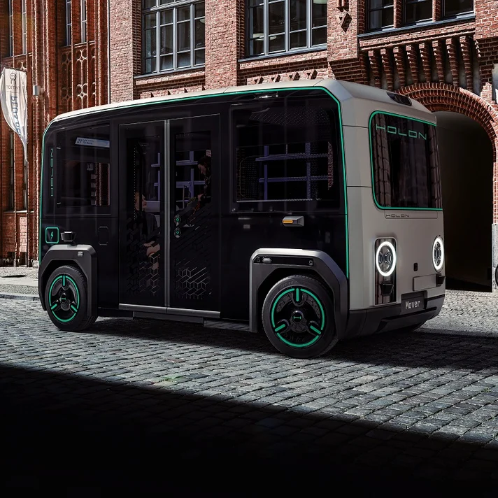 Autonomer Holon Mover parkt auf Kopfsteinpflaster vor historischem Gebäude.