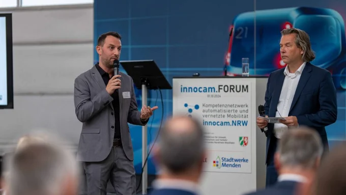 Zwei Männer mit Mikrofonen moderieren gemeinsam das innocam.FORUM auf einer Bühne.