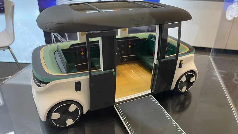 Modell eines autonomen, rechteckigen Fahrzeugs mit Schiebetüren und ausklappbarer Rampe, präsentiert auf einem Tisch beim Mobilitätskongress.