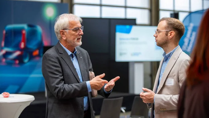 Zwei Männer unterhalten sich bei einer Fachveranstaltung vor dem Hintergrund von Displays und Infotafeln.