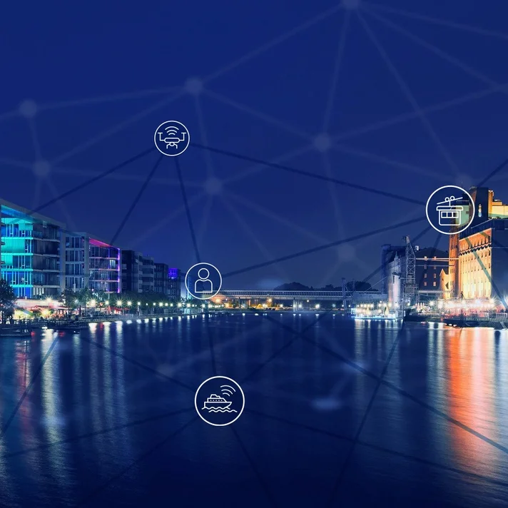 Nächtliche, beleuchtete Panoramaansicht der neunen Innenhafens der Stadt Duisburg im dunklen Blauton mit Lichtakzenten, mit modernen Gebäuden an den Ufern rechts und links, deren Licht sich im Wasser spiegelt. Im Vordergrund sind Icons der automatisierten und vernetzten Mobilität zu sehen, die mit Linien Netzwerk miteinander verbunden sind. 