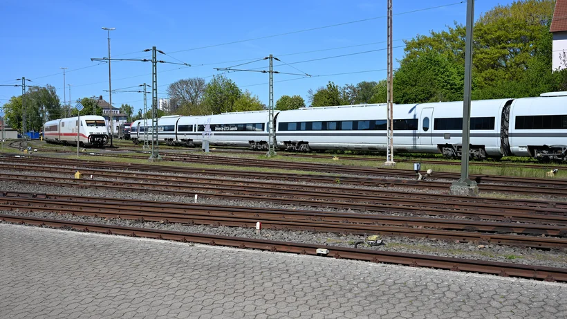 Mehrteiliger weißer Hochgeschwindigkeitszug auf Gleisen vor blauem Himmel und Gebäuden