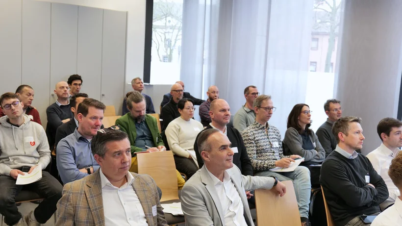 Gruppe von Menschen sitzt in einem Raum auf Stühlen und hört aufmerksam zu