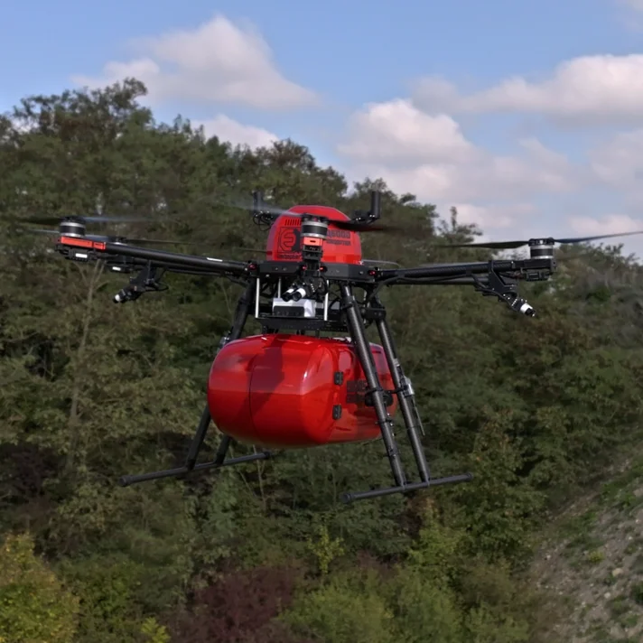 Rote Drohne mit sechs Rotoren fliegt über bewaldetes und bewachsenes Gelände