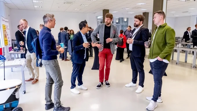 Mehrere Personen stehen in einem hellen, modernen Raum und unterhalten sich in kleinen Gruppen, einige halten Becher in der Hand.