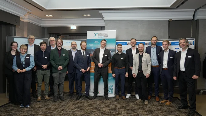 Gruppefoto von Personen in Business-Kleidung steht vor Bannern mit Logos und Texten zum innocam.NRW Mobility Meeting in einem Konferenzraum.