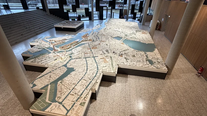 Großes dreidimensionales Stadtmodell mit Wasserflächen in einem modernen Innenraum mit Treppe und Holzverkleidung