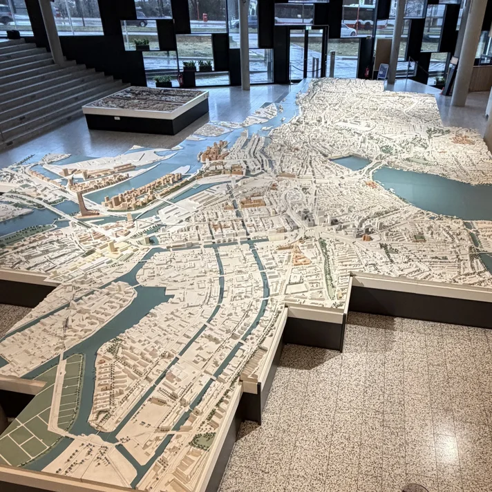 Großes dreidimensionales Stadtmodell mit Wasserflächen in einem modernen Innenraum mit Treppe und Holzverkleidung