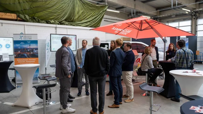 Mehrere Personen im Gespräch an Infoständen in einer Halle mit Bannern und Infomaterial.