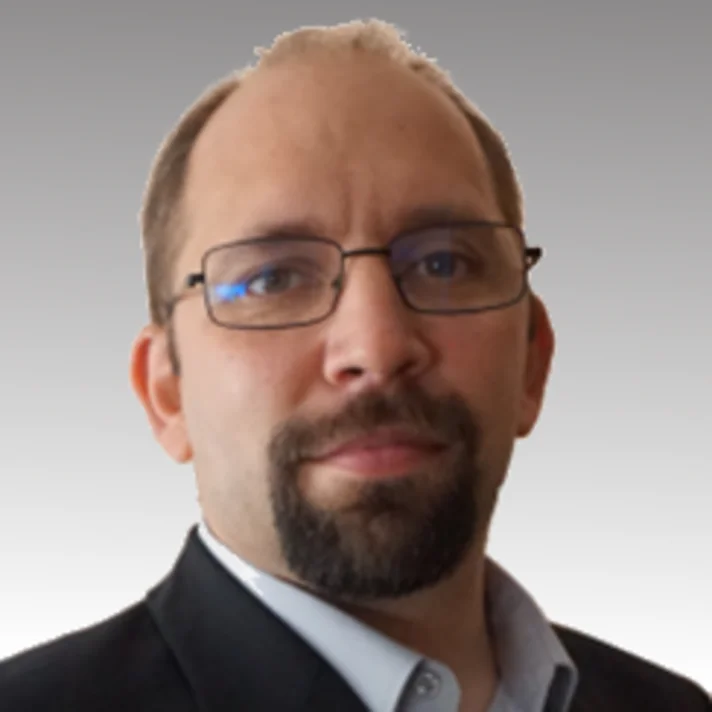 Porträt von Nils Malzahn mit Brille, brauen, kurzen Haaren, dunklem Bart in einem blauen Hemd und schwarzem Sakko.