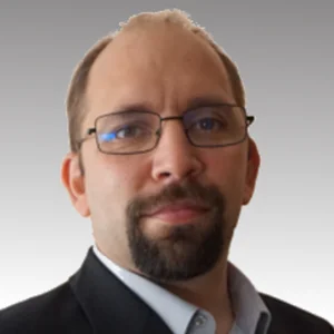 Porträt von Nils Malzahn mit Brille, brauen, kurzen Haaren, dunklem Bart in einem blauen Hemd und schwarzem Sakko.