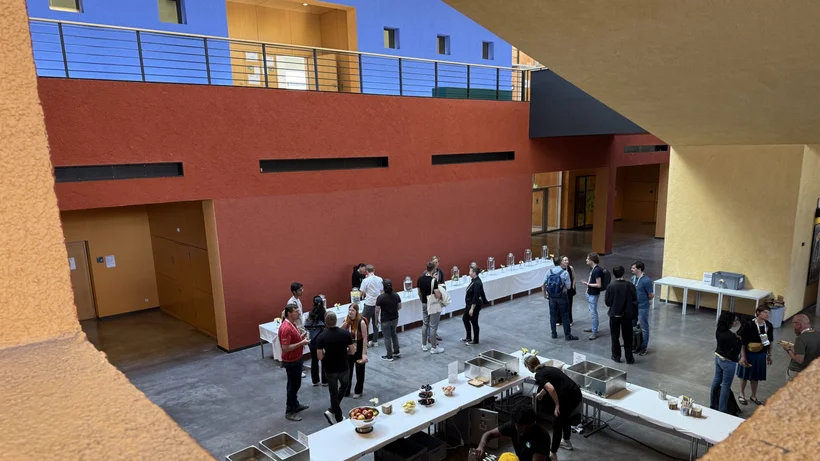 Von einer Galerie aus aufgenommenes Foto eines hohen Innenraums, in der unteren eben stehen Konferenzbesucher um ein Buffet herum und unterhalten sich.