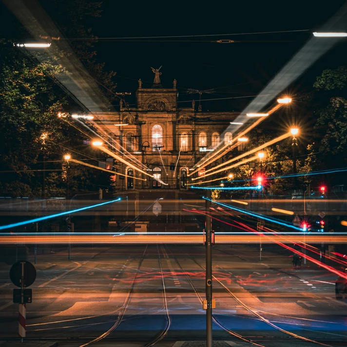 Nachtaufnahme eines historischen Gebäudes mit Lichtspuren von Fahrzeugen und Straßenlaternen im Vordergrund
