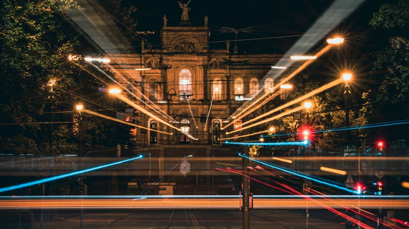Nachtaufnahme eines historischen Gebäudes mit Lichtspuren von Fahrzeugen und Straßenlaternen im Vordergrund