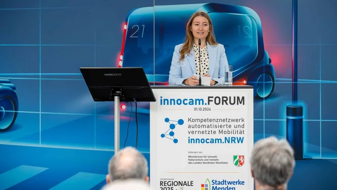 Rednerin spricht beim innocam.FORUM an einem Pult mit Logo und großem Hintergrundmotiv eines Fahrzeugs.