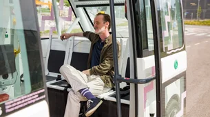 Ein Mann sitzt entspannt im Innenraum eines modernen, automatisierten Busses mit offenen Türen.
