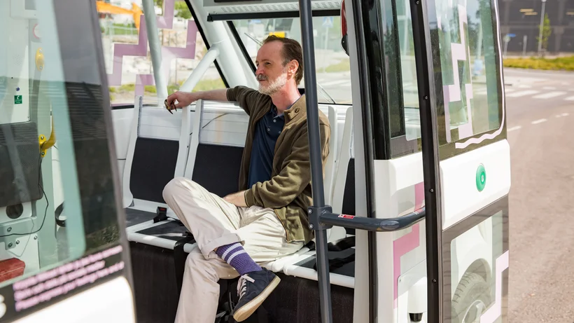 Ein Mann sitzt entspannt im Innenraum eines modernen, automatisierten Busses mit offenen Türen.