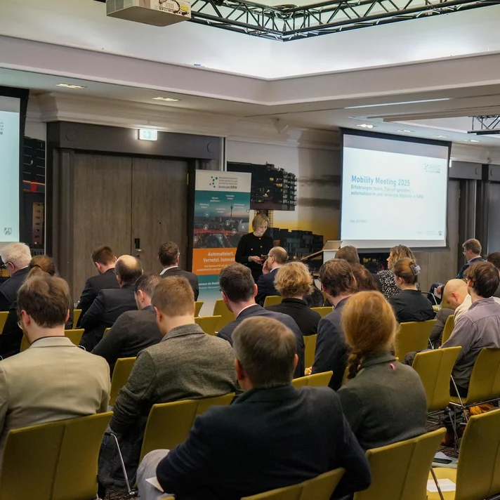 Teilnehmende sitzen in einem Konferenzraum bei der innocam.NRW Mobility Meeting Veranstaltung, Blick auf die Rückseite der Personen und zwei Projektionsflächen vorne.