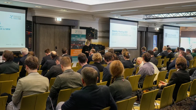 Teilnehmende sitzen in einem Konferenzraum bei der innocam.NRW Mobility Meeting Veranstaltung, Blick auf die Rückseite der Personen und zwei Projektionsflächen vorne.