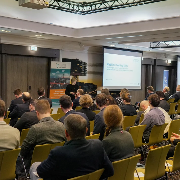 Teilnehmende sitzen in einem Konferenzraum bei der innocam.NRW Mobility Meeting Veranstaltung, Blick auf die Rückseite der Personen und zwei Projektionsflächen vorne.