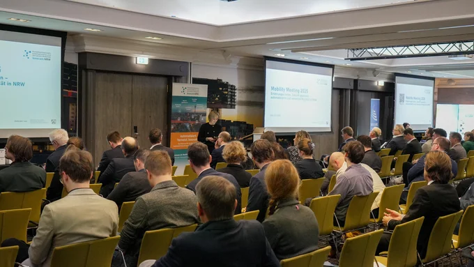 Teilnehmende sitzen in einem Konferenzraum bei der innocam.NRW Mobility Meeting Veranstaltung, Blick auf die Rückseite der Personen und zwei Projektionsflächen vorne.