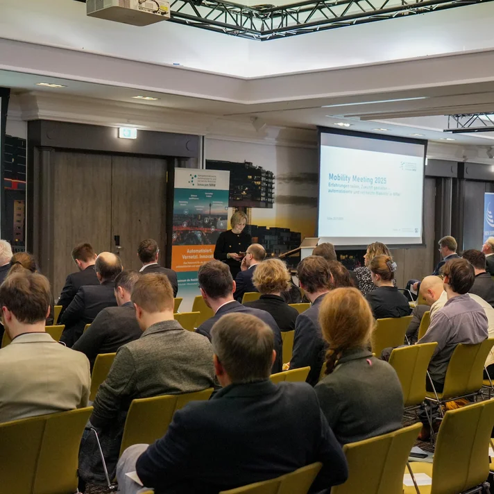Teilnehmende sitzen in einem Konferenzraum bei der innocam.NRW Mobility Meeting Veranstaltung, Blick auf die Rückseite der Personen und zwei Projektionsflächen vorne.
