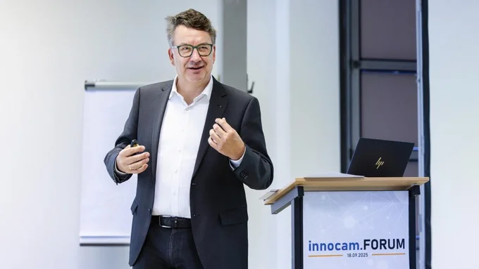 Mann in dunklem Anzug und weißem Hemd hält Präsentation am Rednerpult mit Schild 'innocam.FORUM 18.01.2025'.