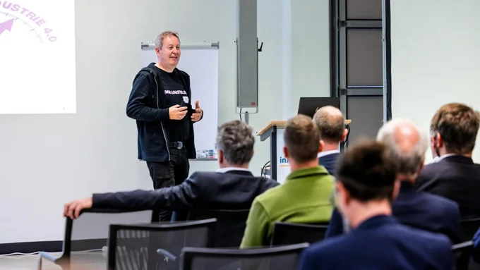 Ein Mann in schwarzer Kleidung steht vor einer Gruppe sitzender Zuhörer und hält eine Präsentation beim innocam.FORUM zur Güterlogistik 2025.