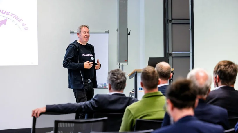 Ein Mann in schwarzer Kleidung steht vor einer Gruppe sitzender Zuhörer und hält eine Präsentation beim innocam.FORUM zur Güterlogistik 2025.