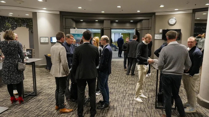 Mehrere Personen stehen in kleinen Gruppen in einem Konferenzraum an Stehtischen und unterhalten sich. 