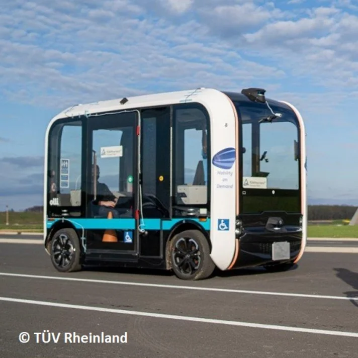 Fahrradfahrer-Dummy vor einem autonomen Shuttlebus auf einem Testgelände.