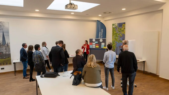 Gruppe diskutiert in Workshopraum vor Pinnwand mit beschrifteten Karten.