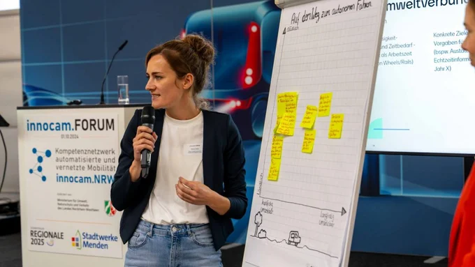 Frau präsentiert Workshop-Ergebnisse zum autonomen Fahren an einem Flipchart mit beschrifteten Haftnotizen.
