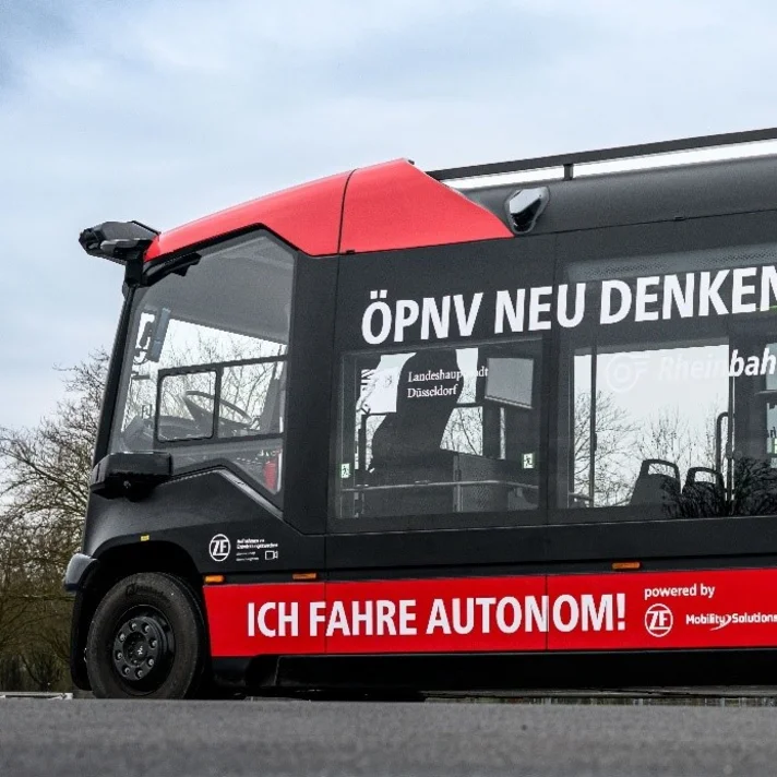 Ein schwarz-roter autonomer Kleinbus mit großem Schriftzug „ÖPNV neu denken“ und Logos von ZF und Rheinbahn.