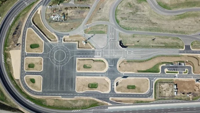 Überblick über ein weitläufiges Testfeld mit verschiedenen Straßentypen, Kreuzungen, einem Kreisverkehr und Parkflächen zur Erprobung von Verkehrsszenarien.