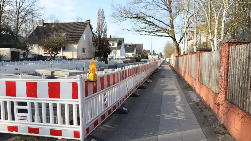 Absperrung mit rot-weißen Warnbaken auf einem Gehweg in einem Wohngebiet; der Gehweg ist dadurch stark verengt.