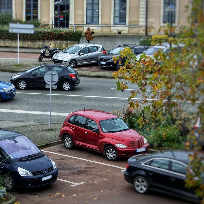 Blick auf eine belebte Straßenkreuzung mit mehreren parkenden und fahrenden Autos sowie einem Fußgänger auf dem Bürgersteig.